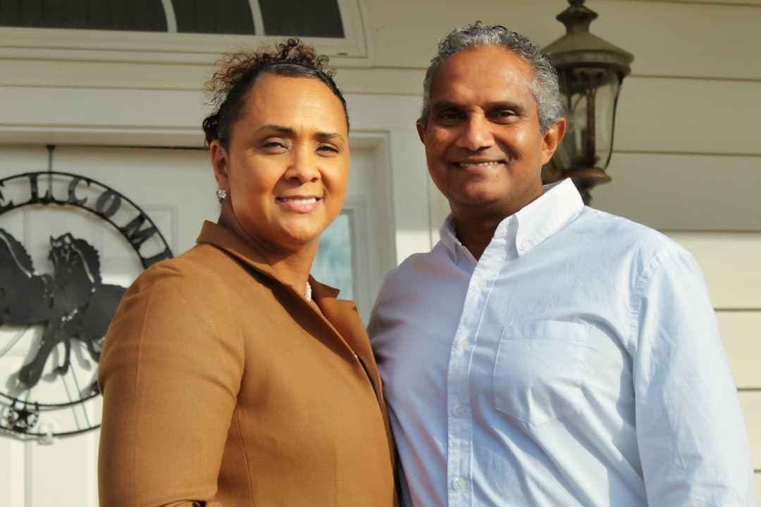 A happy couple stands proudly on the porch of their new house, holding up the keys to their front door, symbolizing a successful home purchase.