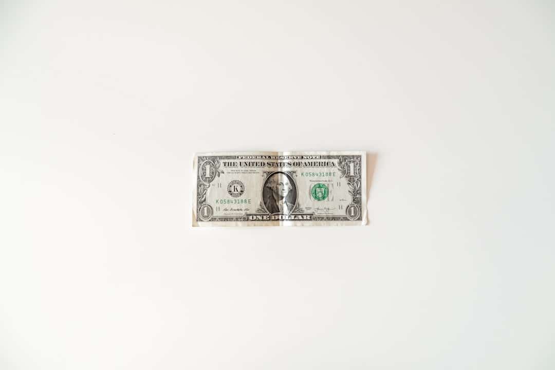 A small model house sits on a stack of money against a clean, modern background, symbolizing home equity and savings from reduced commissions.