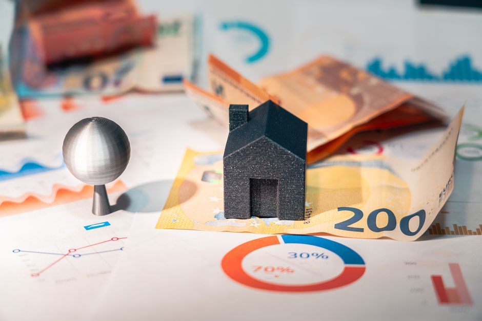 A minimalist photo of a small model home sitting on top of a large stack of cash, illustrating the high financial costs and commissions associated with selling a house.