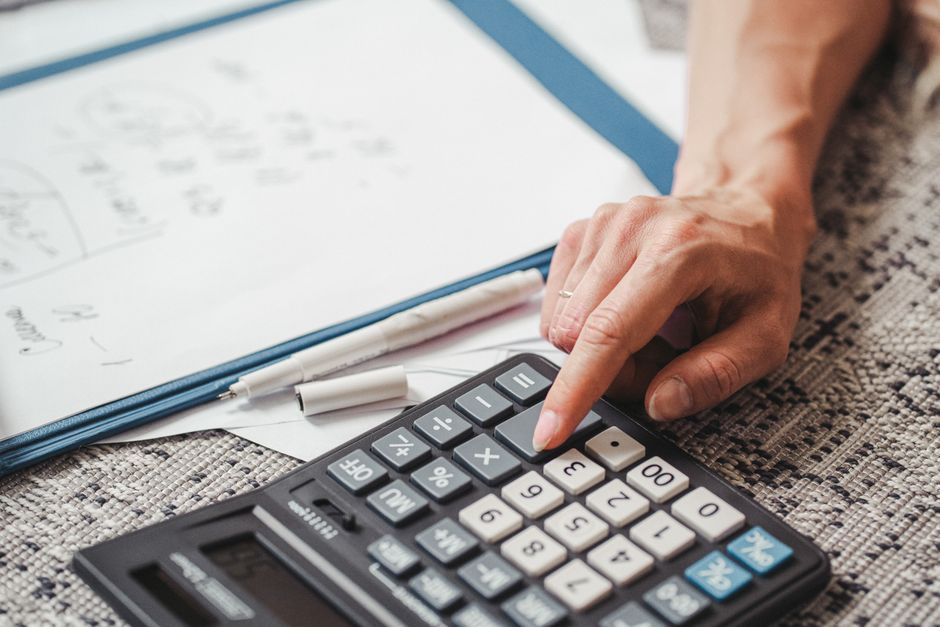 Person sits at a modern desk, seriously reviewing financial paperwork with a calculator nearby, representing the complexit...